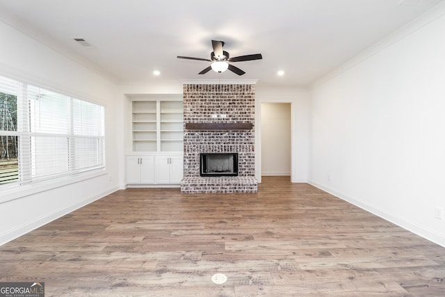 unfurnished living room featuring visible vents, ornamental molding, built in features, wood finished floors, and a brick fireplace