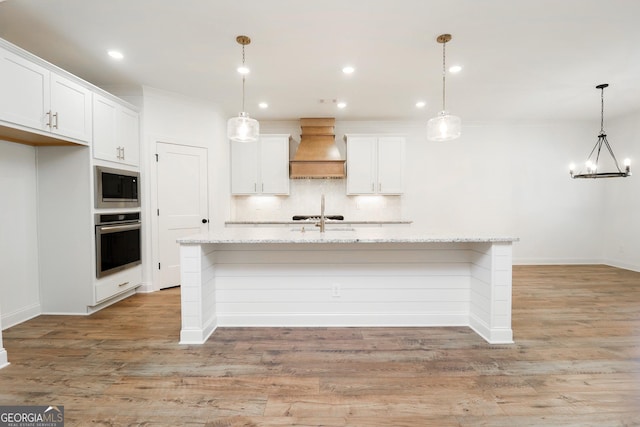 kitchen featuring a center island with sink, light wood-style flooring, stainless steel appliances, custom range hood, and tasteful backsplash