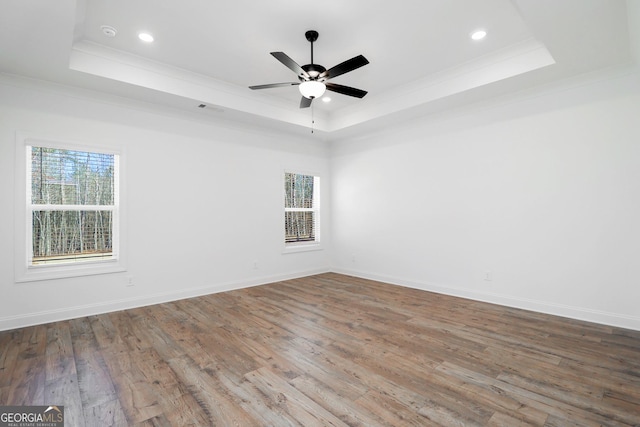 empty room with wood finished floors, baseboards, recessed lighting, ornamental molding, and a raised ceiling