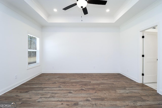 spare room featuring a tray ceiling, baseboards, and dark wood-style flooring