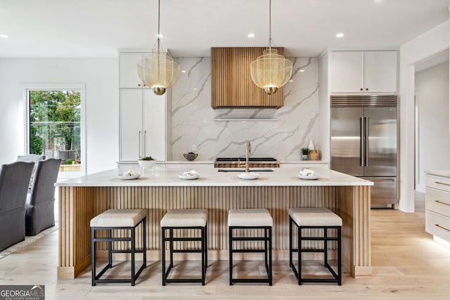 kitchen with backsplash, white cabinets, hanging light fixtures, light hardwood / wood-style flooring, and stainless steel appliances