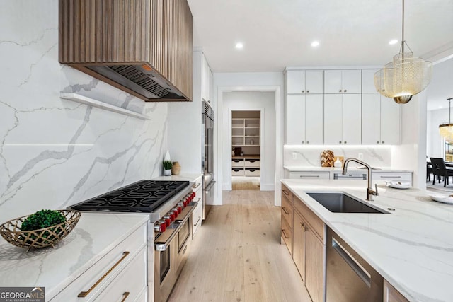 kitchen with sink, premium range hood, pendant lighting, high quality appliances, and white cabinets