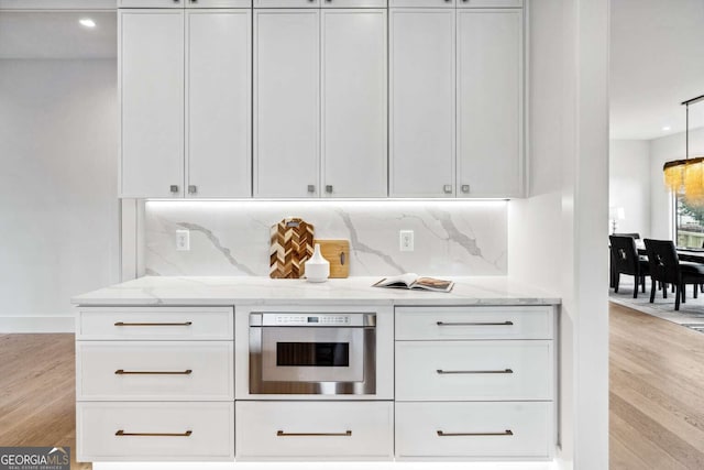 kitchen featuring white cabinets, stainless steel oven, light stone countertops, and light hardwood / wood-style floors