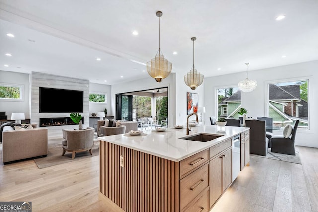 kitchen featuring light wood-type flooring, a large fireplace, sink, decorative light fixtures, and a center island with sink