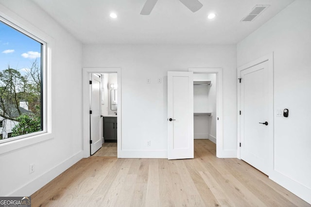 unfurnished bedroom with light wood-type flooring, ceiling fan, a spacious closet, connected bathroom, and a closet