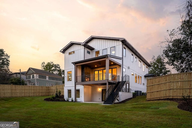 back house at dusk with a lawn, a balcony, and central AC unit