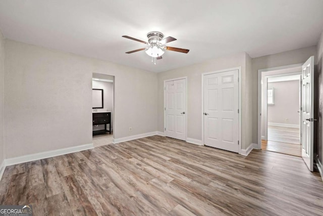 unfurnished bedroom with light hardwood / wood-style floors, multiple closets, ensuite bath, and ceiling fan