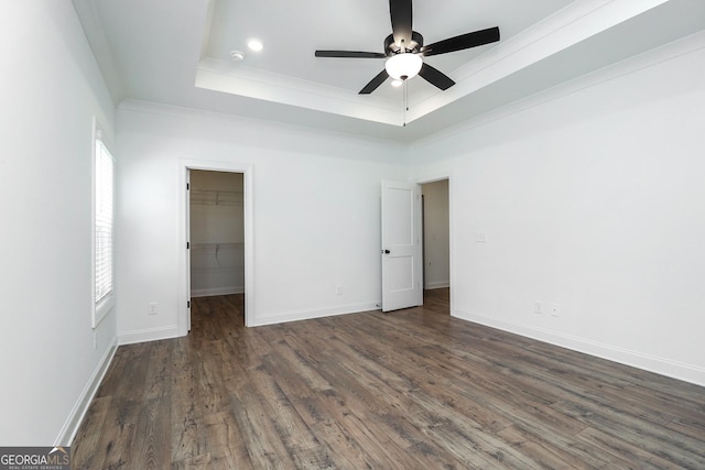 unfurnished bedroom with a walk in closet, baseboards, ornamental molding, wood finished floors, and a raised ceiling