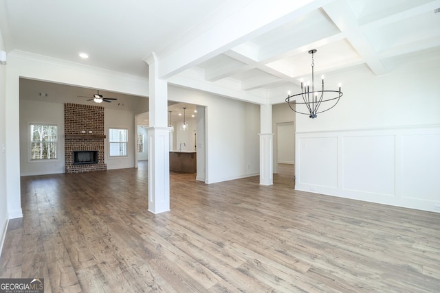 unfurnished dining area featuring light wood-type flooring, beamed ceiling, ceiling fan with notable chandelier, coffered ceiling, and a fireplace