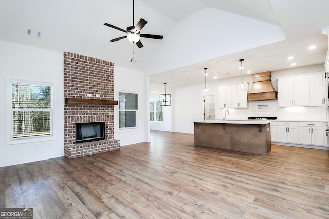 kitchen with visible vents, custom exhaust hood, stovetop, light wood-style flooring, and open floor plan