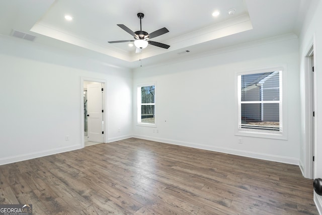 empty room featuring visible vents, baseboards, a tray ceiling, and wood finished floors