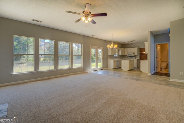 unfurnished living room with light carpet, a textured ceiling, and ceiling fan with notable chandelier