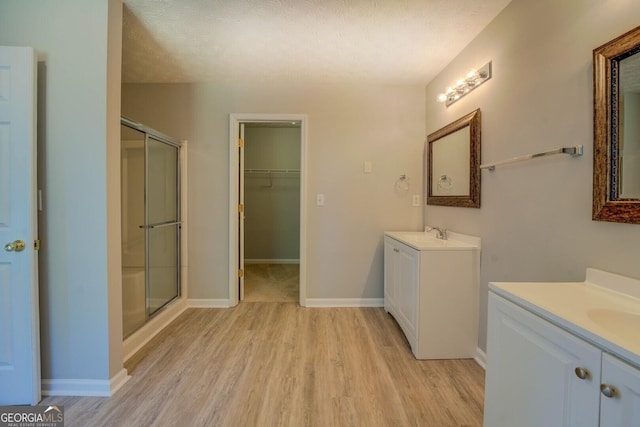 full bathroom with wood finished floors, a shower stall, two vanities, baseboards, and a textured ceiling
