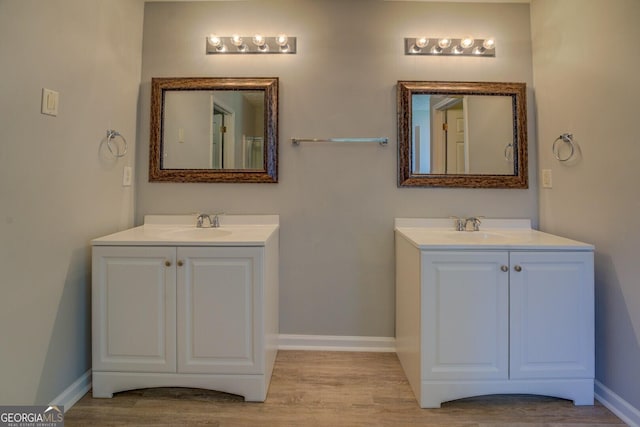bathroom featuring two vanities, wood finished floors, and baseboards