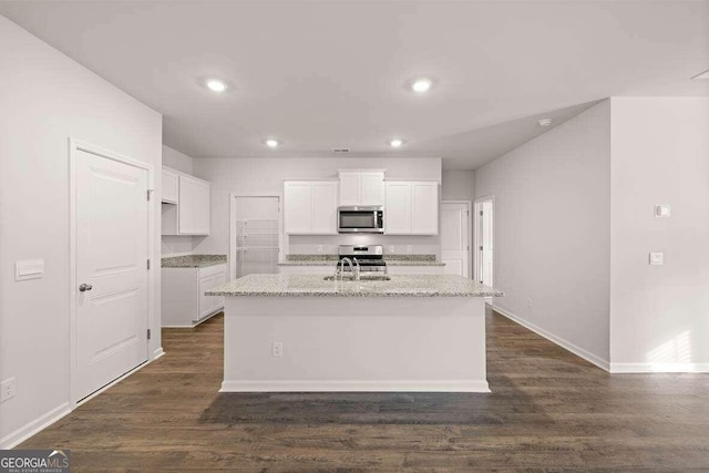 kitchen with white cabinetry, appliances with stainless steel finishes, light stone countertops, and an island with sink