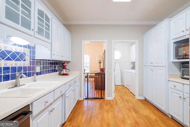 kitchen with sink, crown molding, white cabinetry, washer and dryer, and light hardwood / wood-style floors