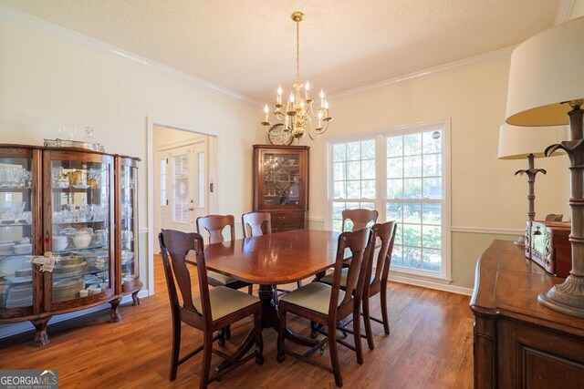 dining area featuring dark wood-type flooring, a textured ceiling, crown molding, and an inviting chandelier