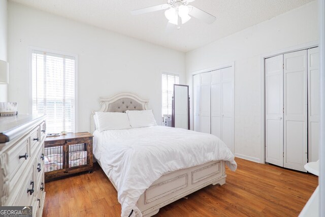 bedroom featuring multiple closets, hardwood / wood-style floors, a textured ceiling, and ceiling fan