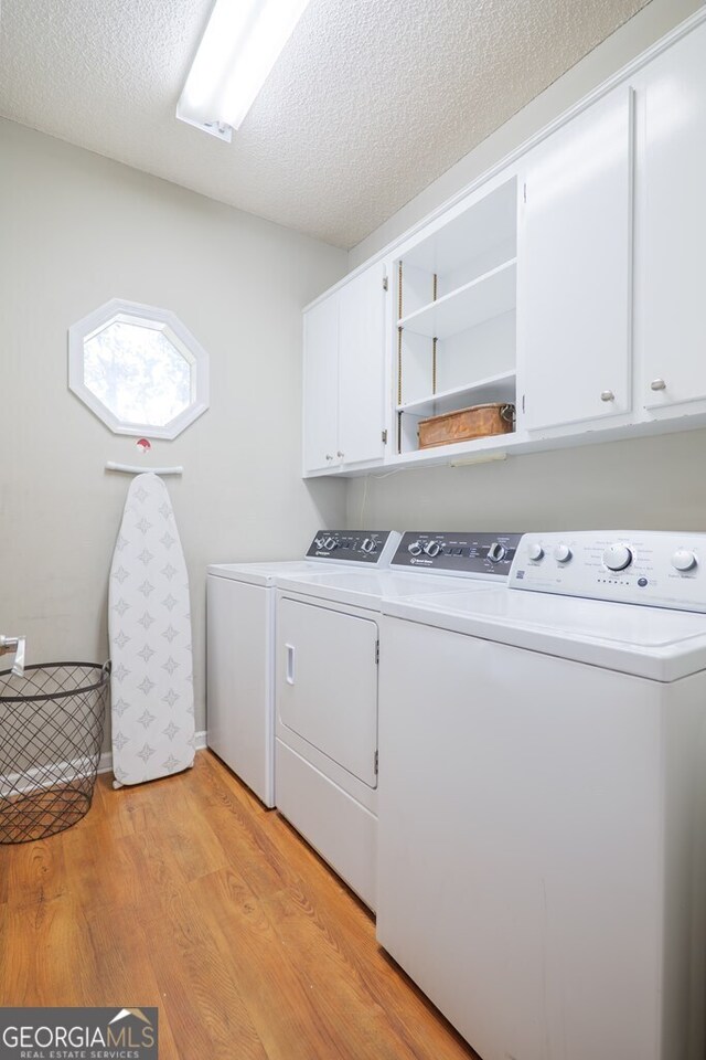 washroom featuring cabinets, light hardwood / wood-style flooring, a textured ceiling, and washer and clothes dryer