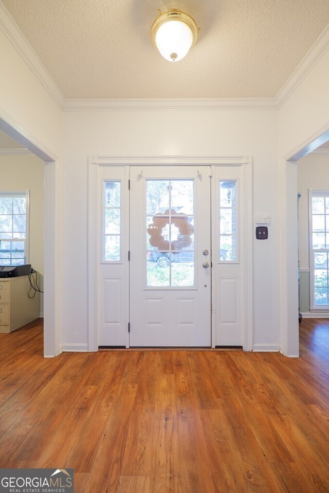 foyer with crown molding, a healthy amount of sunlight, hardwood / wood-style flooring, and a textured ceiling