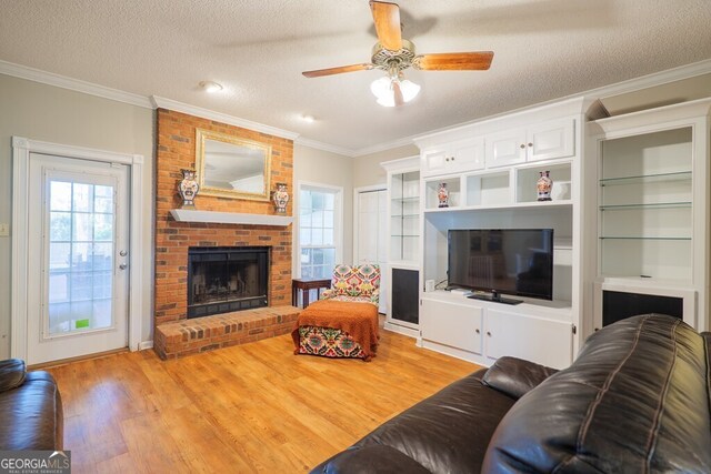 living room with crown molding, light wood-type flooring, a textured ceiling, a fireplace, and ceiling fan