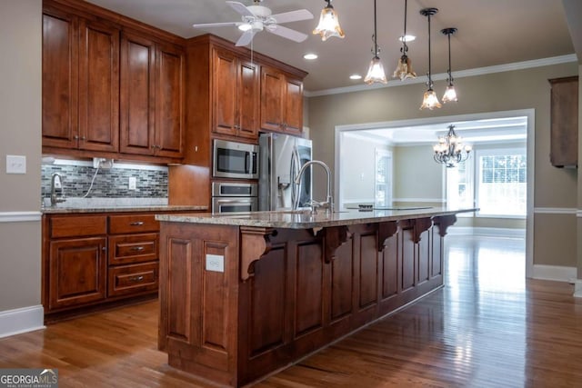 kitchen featuring dark hardwood / wood-style floors, an island with sink, crown molding, appliances with stainless steel finishes, and light stone counters