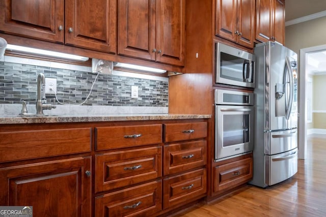 kitchen featuring stainless steel appliances, backsplash, sink, crown molding, and light hardwood / wood-style floors