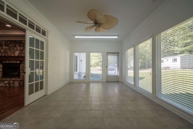 unfurnished sunroom featuring a stone fireplace and ceiling fan