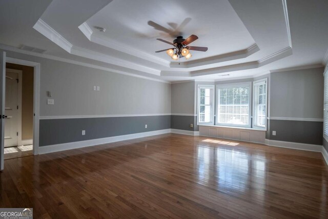 empty room with ceiling fan, ornamental molding, a tray ceiling, and dark hardwood / wood-style floors