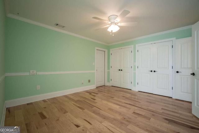 unfurnished bedroom featuring ceiling fan, ornamental molding, light wood-type flooring, and two closets