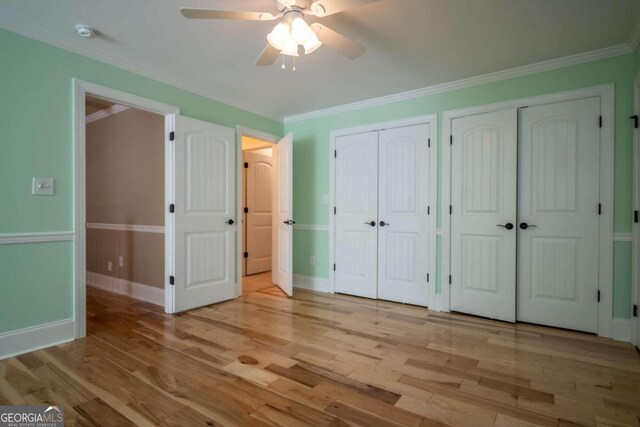 unfurnished bedroom featuring light hardwood / wood-style flooring, ornamental molding, two closets, and ceiling fan