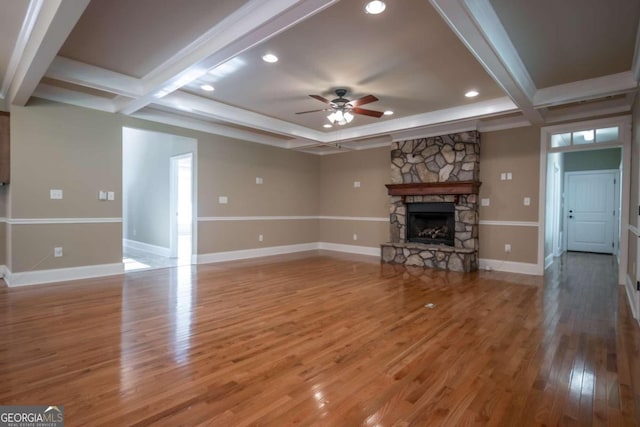 unfurnished living room featuring a stone fireplace, hardwood / wood-style floors, beam ceiling, and ceiling fan