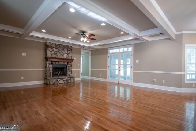 unfurnished living room with a stone fireplace, french doors, ornamental molding, and wood-type flooring