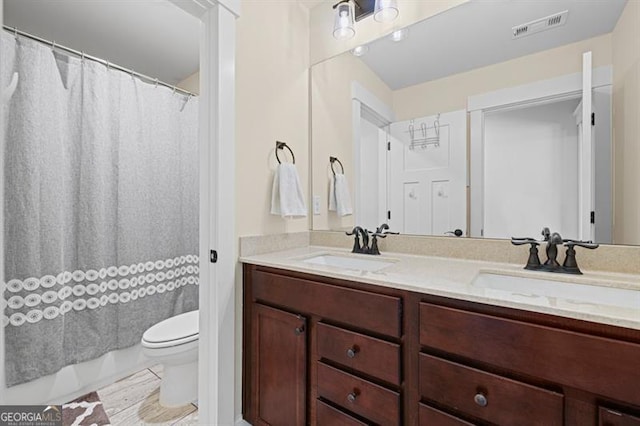 full bath with toilet, double vanity, a sink, and visible vents