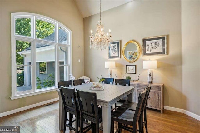 dining space featuring an inviting chandelier, light wood-type flooring, and vaulted ceiling