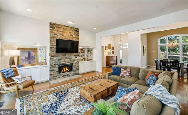 living room with a stone fireplace, a chandelier, and wood-type flooring