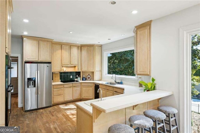 kitchen with kitchen peninsula, stainless steel fridge, light brown cabinetry, sink, and light hardwood / wood-style flooring