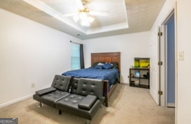 bedroom featuring light colored carpet, a raised ceiling, and ceiling fan