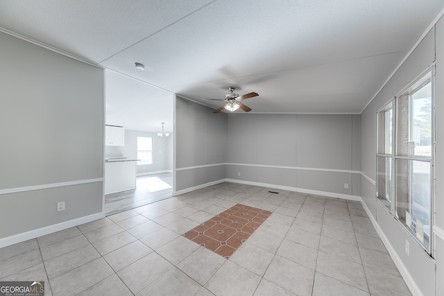 spare room featuring a textured ceiling, light tile patterned flooring, plenty of natural light, and ceiling fan with notable chandelier