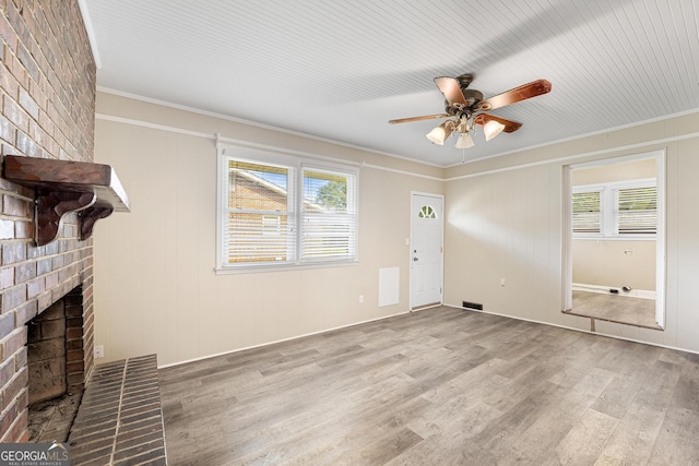 unfurnished living room with light hardwood / wood-style flooring, ornamental molding, a wealth of natural light, and a brick fireplace