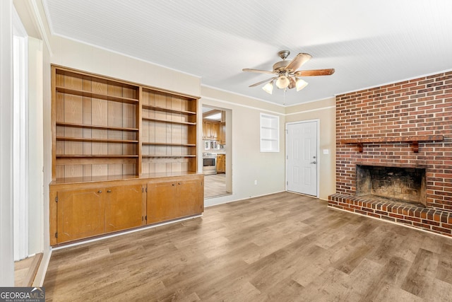 unfurnished living room with ceiling fan, ornamental molding, a brick fireplace, and light wood-type flooring