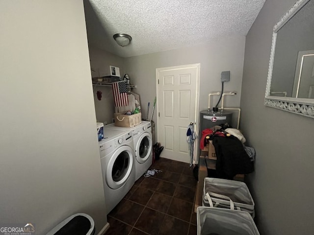 washroom with a textured ceiling, water heater, washing machine and clothes dryer, and dark tile patterned flooring