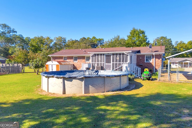 rear view of property with a yard, a shed, a covered pool, and a sunroom