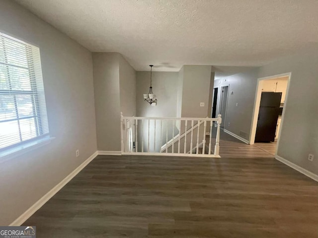 empty room featuring an inviting chandelier, dark hardwood / wood-style floors, and a textured ceiling