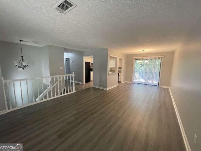 spare room featuring dark wood-type flooring, a textured ceiling, and an inviting chandelier