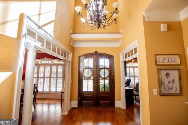 entryway with a notable chandelier, decorative columns, crown molding, dark wood-type flooring, and french doors