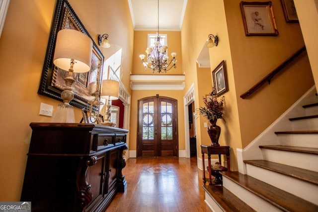 foyer entrance with an inviting chandelier, french doors, hardwood / wood-style flooring, and crown molding