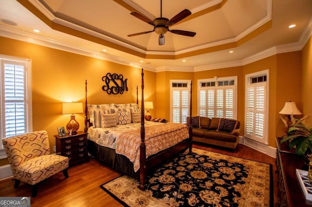 bedroom with hardwood / wood-style floors, crown molding, multiple windows, and a tray ceiling