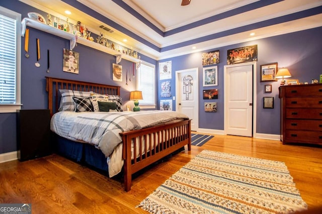 bedroom with ornamental molding, hardwood / wood-style flooring, and a tray ceiling