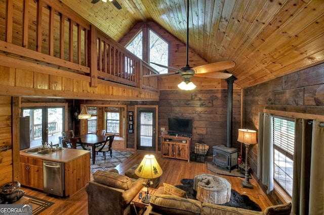 living room featuring light wood-style flooring, a wood stove, a ceiling fan, and wood ceiling